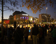 Überblicksfoto von der Gedenkkundgebung auf dem Platz der Alten Synagoge in Freiburg. Im Dunkeln stehen mehrere Hundert auf dem Platz. Im Hintergrund ist das Stadttheater zu erkennen. "Wir gedenken den Opfern der Shoa" steht auf einem Plakat.