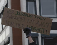 Eine Hand hält ein Pappschild, auf dem in Großbuchstaben steht: Wer Journalist*innen angreift hat Angst vor der Wahrheit!