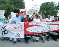 Protestmarsch mit vielen Männern und Frauen in Karatschi 2019. Sie tragen vor sich ein Banner mit den Logos der Gewerkschaftsvereinigungen