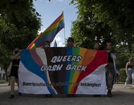 Fronttransparent mit regenbogenfarben und ergänzend durch trans- und bipoc-solidarische Farben. "Queers bash back - Queerfeindlichkeit erkennen und bekämpfen!" steht darauf. Regenbogenfahnen in den ersteh Reihen, links und rechts Bäume vom Schloßplatz.