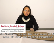 Meitaka Kendall-Lekka Dozentin auf den Marschall Inseln sitzt mit Handschuhen vor einem Tisch, auf dem ein Paddel liegt und erklärt