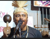 Ein Xukurumann mit Rassel und traditioneller Kopfbedeckung bei der Veranstaltung zur Verkündung der Wahlergebnisse 2018 am Mikro
