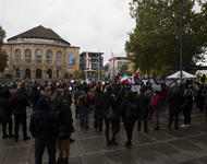 Es ist die Menschenmenge auf dem Platz der Alten Synagoge zu sehen. Mehrere tragen iranische Flaggen (ohne Hohheitsabzeichen), viele halten weiße Schilder in die Höhe. Links im Hintergrund ist das Freiburger Stadttheater zu sehen. 
