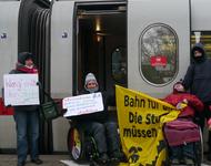 Protestaktion: Zwei Menschen im Rollstuhl und zwei stehende Personen vor einem ICE in Lüneburg
