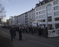 Demonstrationszug in der Friedrichstraße in einer schrägen Seitenansicht. Weißes Fronttransparent weist auf den Mord an Oury Jalloh hin und ein ebenfalls weißes Hochtransparent auf Polizeigewalt insgesamt.