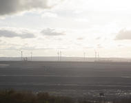 Blick in den Tagebau Inden. Es sind Bagger zu sehen und im Hintergrund Windkraftanlagen. Das Bild ist durch Gegenlicht aufgehellt.