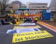 Menschen sitzen und stehen mit Bannern, Fahnen und Schildern vor dem Eingangstor des Atomkraftwerks Emsland.