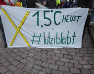 Banner auf dem ein großes gelbes Kreuz zu sehen ist neben der grünen Schrift: "1,5°C heißt #lützibleibt"