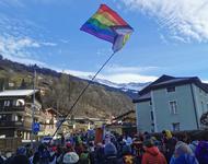 Menschen wandern als große Gruppe nach Davos, im Hintergrund Schnee bedeckte Berge, eine LGBTQIA* Flagge wird geschwenkt.