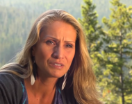 Still from the documentary PLACEnta by Jules Koostachin (2012): The filmmaker talking to an interviewer in front of a forest. She is looking worried and frowns.