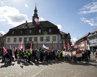 Auf dem Marktplatz in Emmendingen stehen Streikende versammelt, ganz rechts Person mit Megafon zur Menge gerichtet. Es ist leicht bewölkt, aber die Sonne scheint.