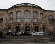 Blick auf das Freiburger Stadttheater. Vor den Toren stehen Demonstrierende aufgereiht mit einem großen Banner, auf dem "We stand with Ukraine" steht. Viele Fahnen der Ukraine sind zu sehen.