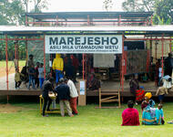 Ausstellung Marejesho am Kilimanjaro - ein Pavillon auf der Wiese mit vielen Besucher*innen. Im Hintergrund Bananenstauden.