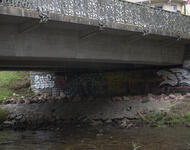 Blick unter die Oberaubrücke. Vorne ist die Dreisam zu sehen, dahinter eine besprühte Wand, darüber die Brücke. Auf der Ebene unter der Brücke sind eine Vielzahl an Steinen eingebracht.