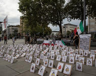 Portraits vieler in der Islamischen Republik Getöteter sind auf dem Boden aufgestellt. Im Hintergrund ist ein Tisch zu sehen, Iran-Fahnen und eine Tavel mit den Gesichter vieler Gefangener.