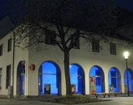 Das frühere Verkehrsamt auf dem Freiburger Rotteckring bei Nacht; die Bögen sind in blaues Licht getaucht; darin steht das Logo von Freiburg 2020