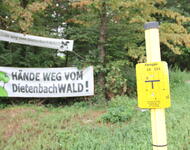 Im Vordergrund Schild der Gashochdruckleitung auf Grünstreifen südlich Munzingerstr. Im Hintergund Transpis gegen neue Trassenführung