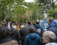 Menschenmenge der Uni Freiburg, zwei Menschen davon mit Jacken mit Uni-Logo, schauen auf zwei Redner*innen. Die eine Person trägt eine rote Verdi-Jacke, die andere eine Warnweste. Am rechten Bildrand ist eine Tafel mit Forderungen der Gewerkschaft zu sehn