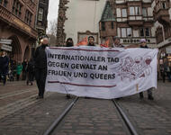 Hochformat. Demospitze mit weißem Transparent mit 5 Leuten, die es halten vor dem Martinstor: "Internationaler Tag gegen Gewalt an Frauen und Queers"