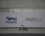 Ein Schild zeigt das Logo der Türkischen Gemeinde in Baden-Württemberg und LEUCHTLINIE, Beratung für Betroffene von rechter Gewalt in Baden-Württemberg