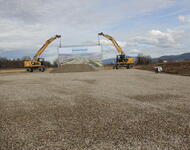 Zwei Bagger auf einem der letzten Baufelder halten ein buntes Modellbild vom neuen Stadtteil Dietenbach hoch. Davor eine Sandhaufen  für Sandwerferei der Politprominenz