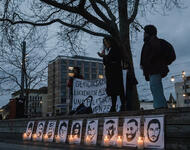 Zwei Menschen stehen auf einer Empore auf dem Platz der Alten Synagoge im Dunkeln. Unten sind neun Portraits der Ermordeten von Hanau zu sehen, davor jeweils eine Kerze.