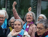 Nach der Urteilsverkündung vom 9. April 2024 vor dem Eurpäischen Gerichtshof für Menschenrechte: Die Gruppe älterer Frauen mit blau-lila Schals. Einige recken triumphierend und mit geöffnetem Mund die Faust empor. Foto © Miriam Künzli / Greenpeace