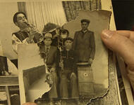 Detailaufnahme auf Hä  nden, die schwarz-weiß Fotos zum Teil zerrissen von Romafamilien
