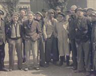 Farbfoto Mai 1945: Gruppenporträt ehemaliger politischer Gefangener im befreiten KZ Dachau. Der Mann mit dem roten Schal ist Jean (Johnny) Vosté, geboren im belgisch besetzten Kongo. Er war Widerstandskämpfer und der einzige Schwarze Gefangene in Dachau.