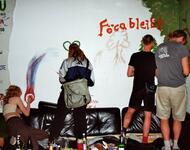 Im alten Raum des FöCas stehen Menschen und bemalen eine Wand. Der Schriftzug "FöCa bleibt" sticht ins Auge.