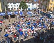 Blick auf den Augustinerplatz von oben. Viele Leute liegen auf mitgebrachten Matten. Die Farbe blau dominiert auf vielen Shirts oder Schirmen der Initiative "ME/CFS Freiburg".