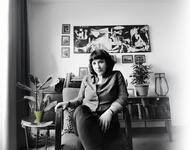 Schwarz-weiß-Portrait von TIna Sanders. Sie sitzt mit überkreuzten Beinen auf einem Sessel in Mitten eines Raumes. Im Hintergrund sind Bilder und Pflanzen zu sehen.