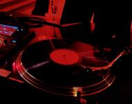 Im Vordergrund ist ein Plattenspieler zu sehen. Im Hintergrund zwei tanzende Menschen im Steinfoyer des Theaters.