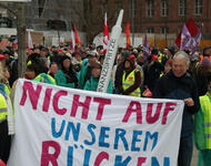 Transparent: Nicht auf unserem Rücken bei Protest gegen geplanten Stellenabbau an Uniklinik Freiburg, am 28.02.2026 am Platz der alten Synagoge; dahinter u.a. eine überdimensionierte Finanzsspritze