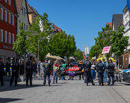 Hinter einer Polizeireihe stehen ein paar antifaschistische Gegendemonstrant*innen mit einem Transparent auf dem "Nazi-Strukturen zerschlagen" steht.