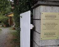 Auf einer Smalen Mauer mit weißem Zaun ist eine goldene Tafel angebracht. Auf dieser finden sich Informationen zur jüdischen Vergangenheit des Markenhofs in drei Sprachen.